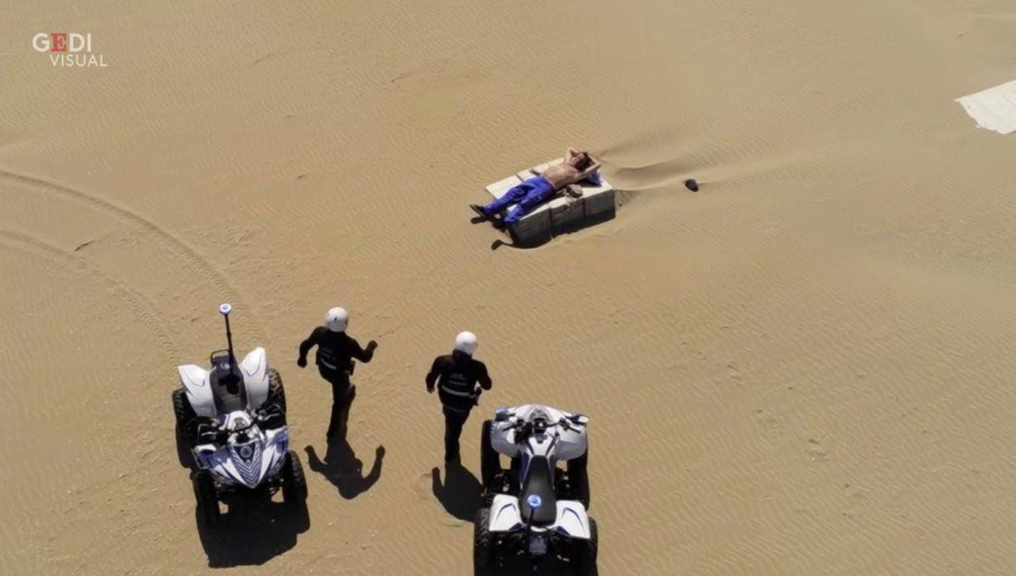 abril 2020 | Rímini, Italia | Un hombre tumbado al sol quieto mientras dos agentes se apresuran a evacuarlo dadas las prohibiciones en la época del coronavirus